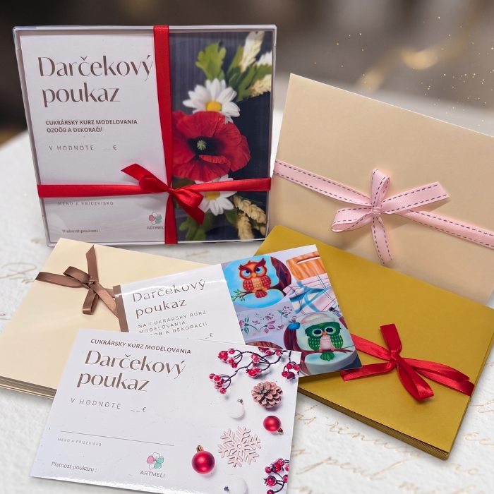 Darčekový poukaz na cukrárske kurzy Artmeli luxusne zabalený v štvorcovej bielej krabičke previazanej výraznou červenou stuhou s mašľou. Na vrchu krabičky je poukaz s fotografiou červeného vlčieho maku a margarétok. Pred krabičkou je voľne položený ďalší poukaz so zimným motívom myšky a snehuliaka, vedľa ktorého leží cukrársky kovový nástroj na modelovanie a živé kvety margarétok.